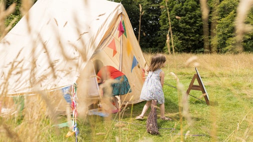 Children explore the dress up tent in the parkland during Lacock's summer of play. One child is riding a broom while the other rummages for something to dress up in.